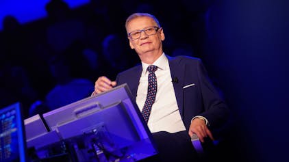„Wer wird Millionär“-Moderator Günther Jauch sitzt während der Quizshow des Kölner TV-Senders RTL auf seinem Stuhl am Pult uns grinst ins Publikum.