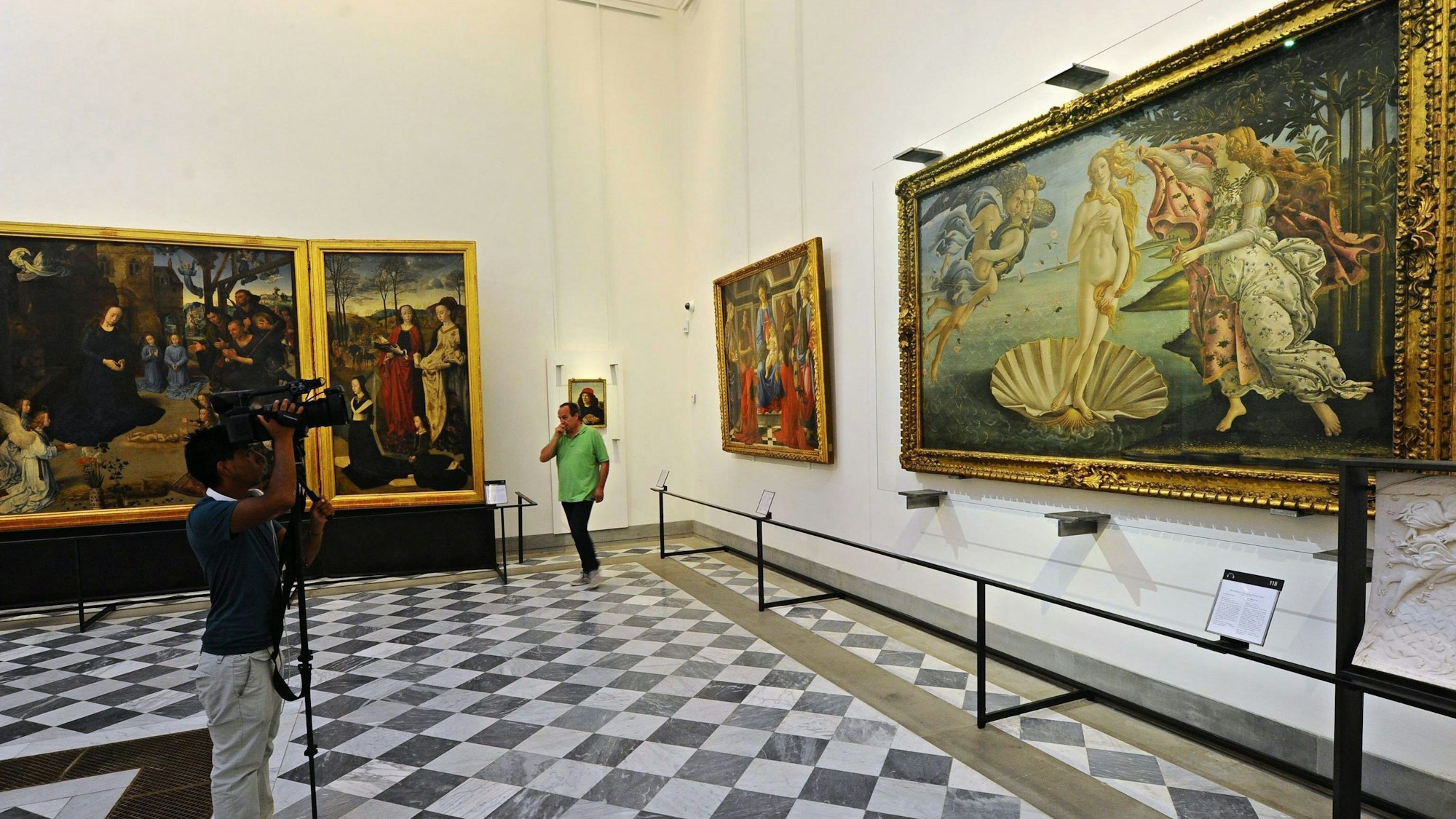 Ein Mann mit Kamera steht in den Uffizien von Florenz vor dem Gemälde.