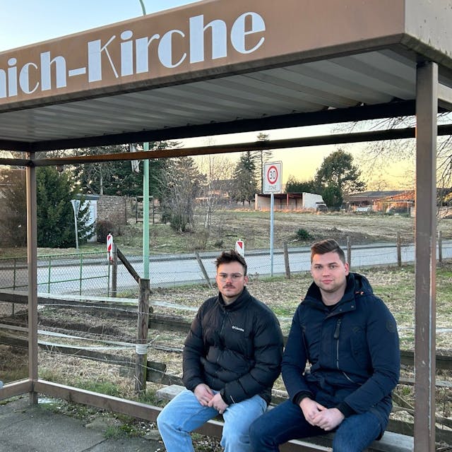 Lennart Bongart und Calvin Köcher sitzen im Haltestellenhäuschen von Morschenich. Sie planen, in ihr altes Dorf zurückzukehren, wenn die Bedingungen stimmen.