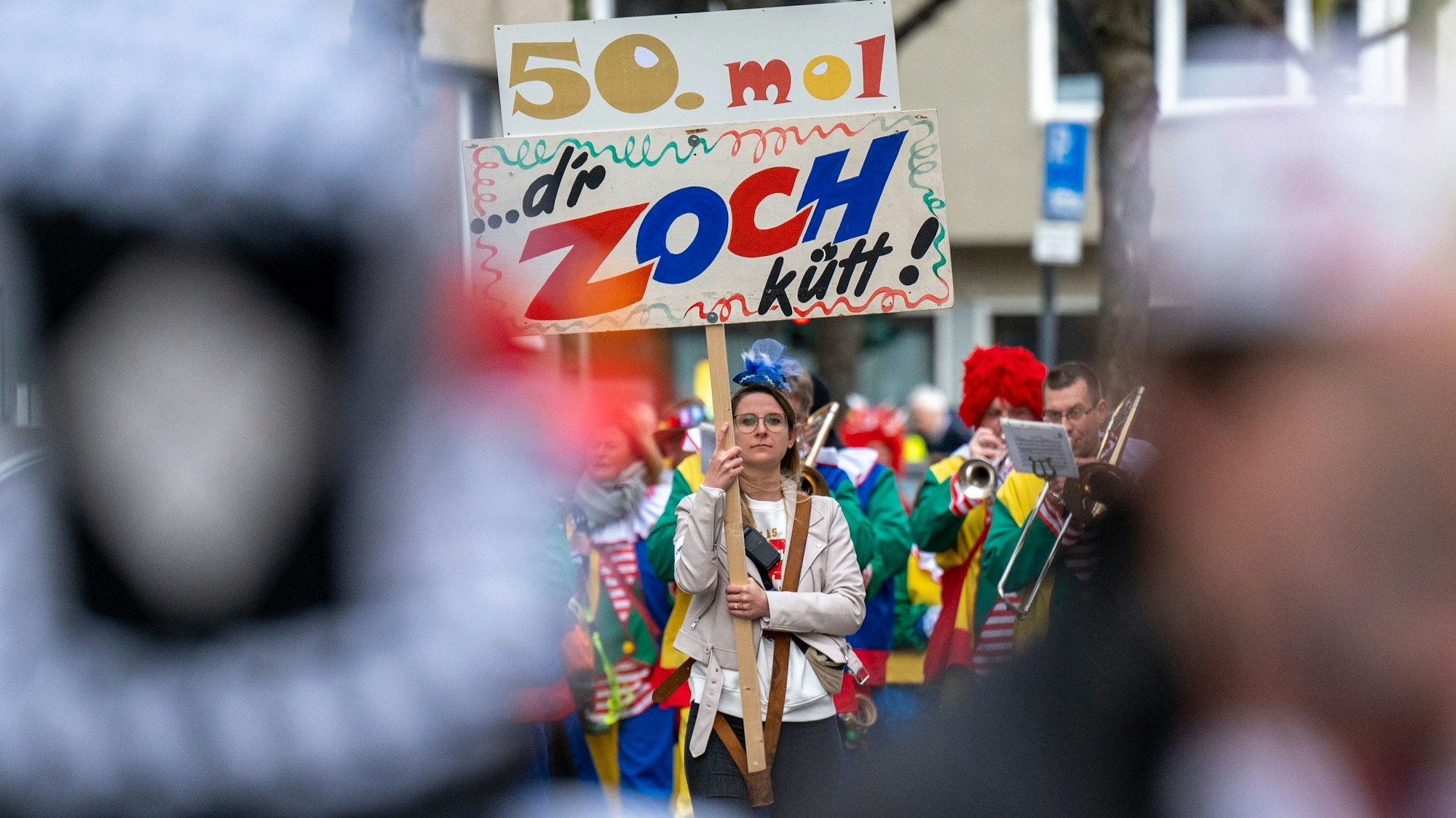 Eine Frau trägt ein Banner mit der Aufschrift: „D'r Zoch kütt“. In Köln-Deutz tut er das zum fünfzigsten Mal.