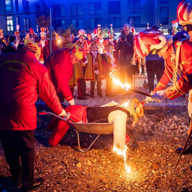 Die Männer der Euskirchener Karnevalsgesellschaft zünden mit einer brennenden Fackel den Nubbel – eine bekleidete Strohpuppe – an, die in einer Schubkarre liegt.