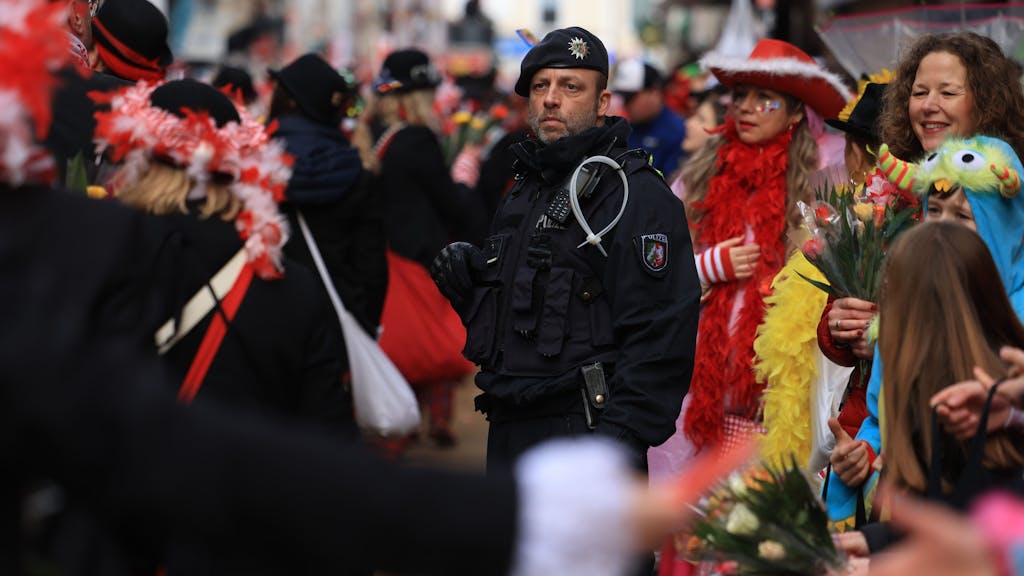 Ein Polizist steht inmitten von Karnevalistinnen und Karnevalisten im Rosenmontagsumzug.