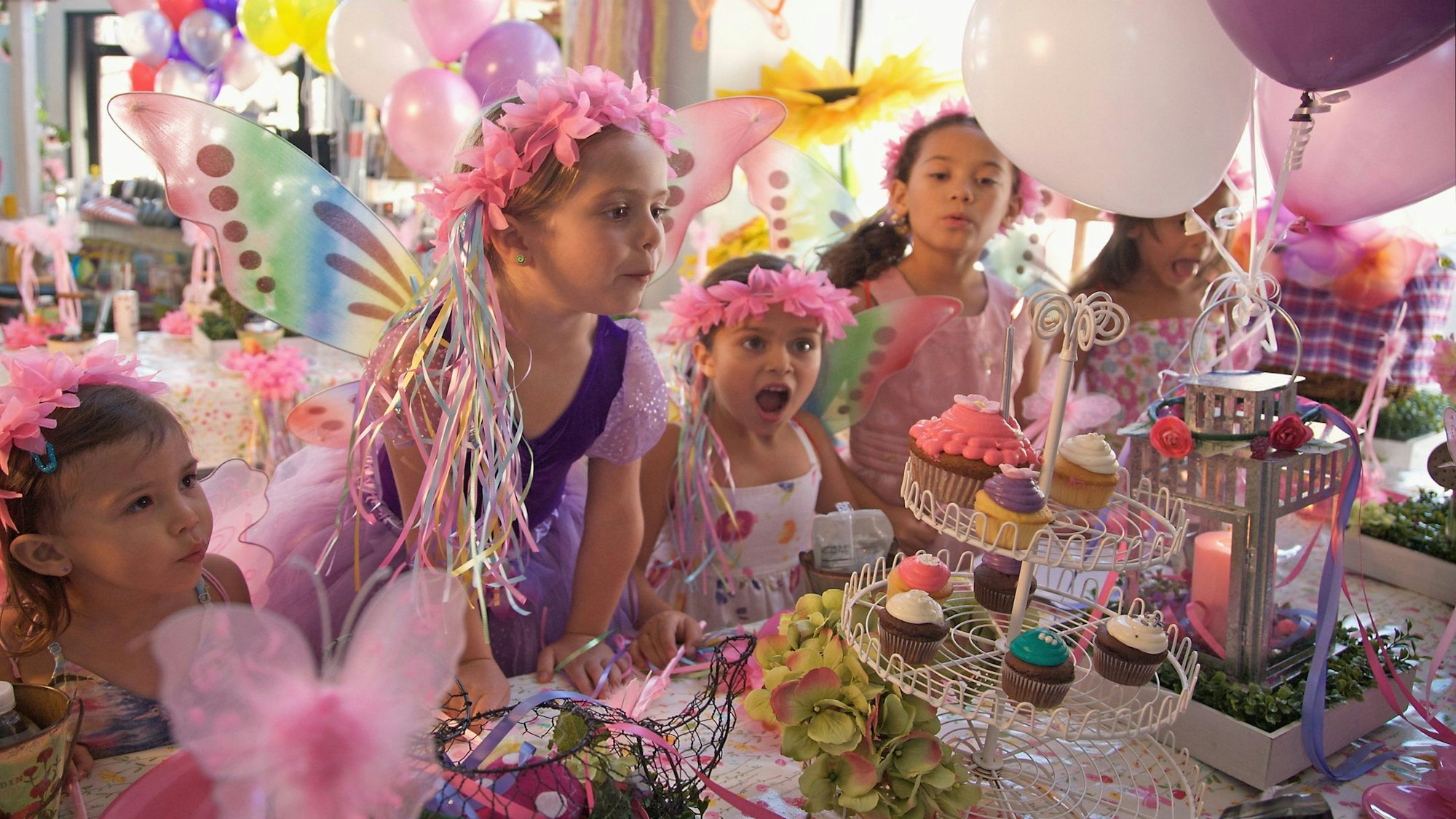 Ein Mädchen im lila Kleid mit Blumenkranz feiert mit ihren Freundinnen Geburtstag.
