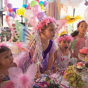 Ein Mädchen im lila Kleid mit Blumenkranz feiert mit ihren Freundinnen Geburtstag.