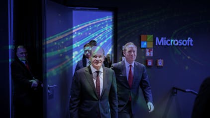 Bundeskanzler Olaf Scholz (SPD) und Microsoft-Präsident Brad Smith auf dem Weg zu einer Pressekonferenz, in der die Investitionspläne des US-Konzerns im Rhein-Erft-Kreis vorgestellt werden. Im Hintergrund ist das Firmenlogo von Microsoft zu sehen, ebenso wie ein Teil einer farbigen Wandpräsentation.