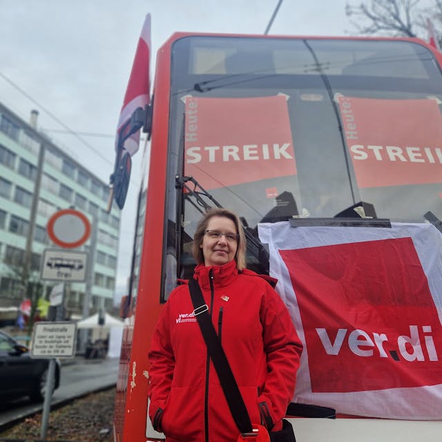 Eine Frau steht vor einer Straßenbahn der KVB. Darauf sind Streik-Plakate zu sehen.