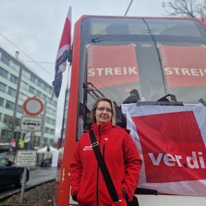 Eine Frau steht vor einer Straßenbahn der KVB. Darauf sind Streik-Plakate zu sehen.