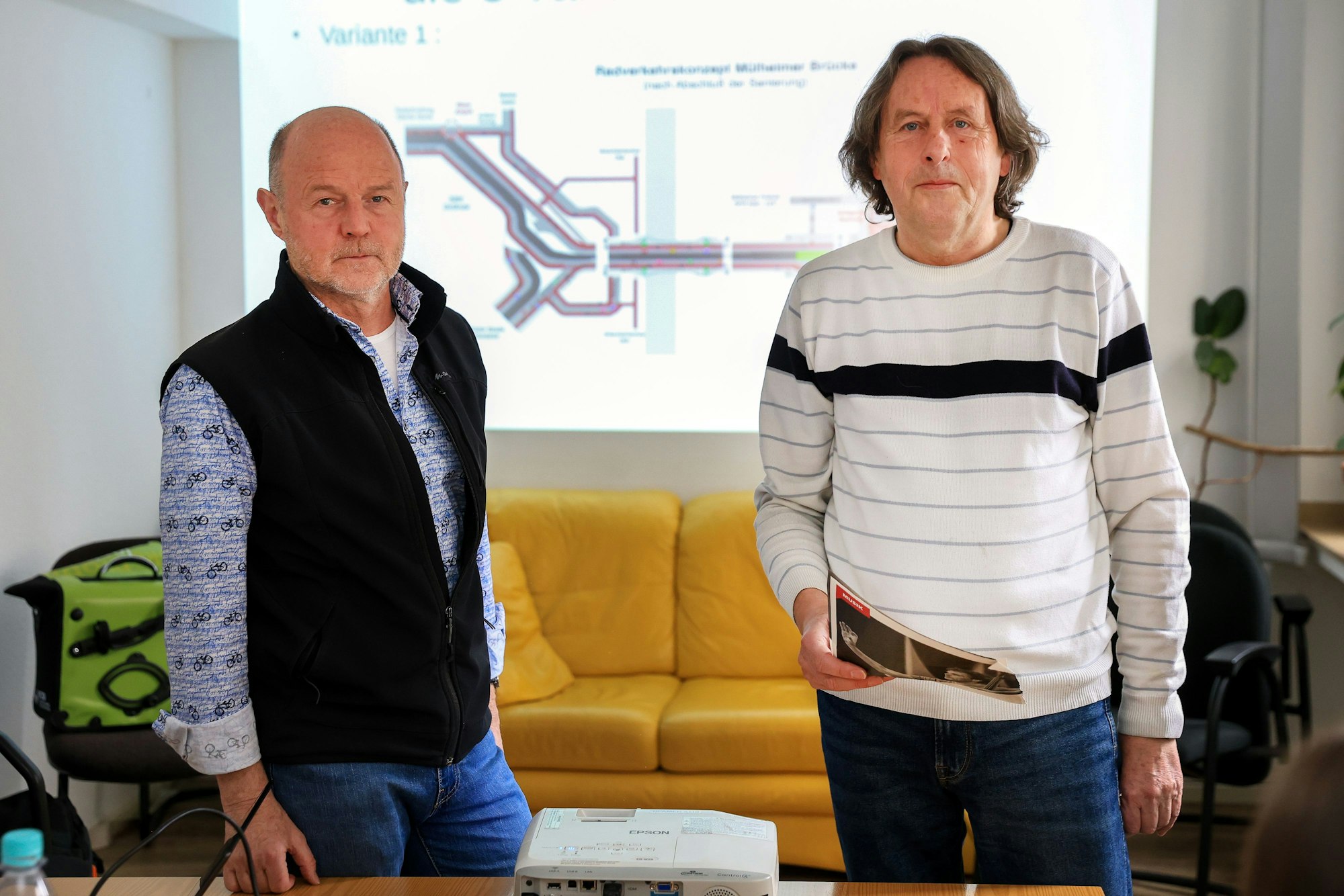 Günter Hermkes und Roland Schüler von der neugegründeten Initiative „Neue Mülheimer Brücke“ stehen vor einem Sofa.