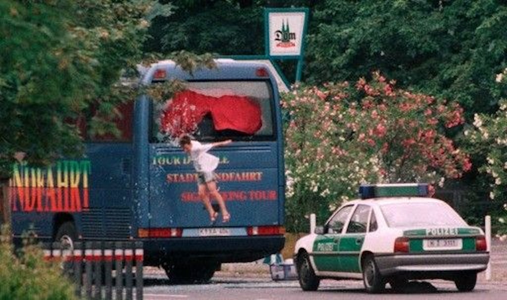 Ein Junge springt durch das zerschossene Heckfenster eines Reisebusses