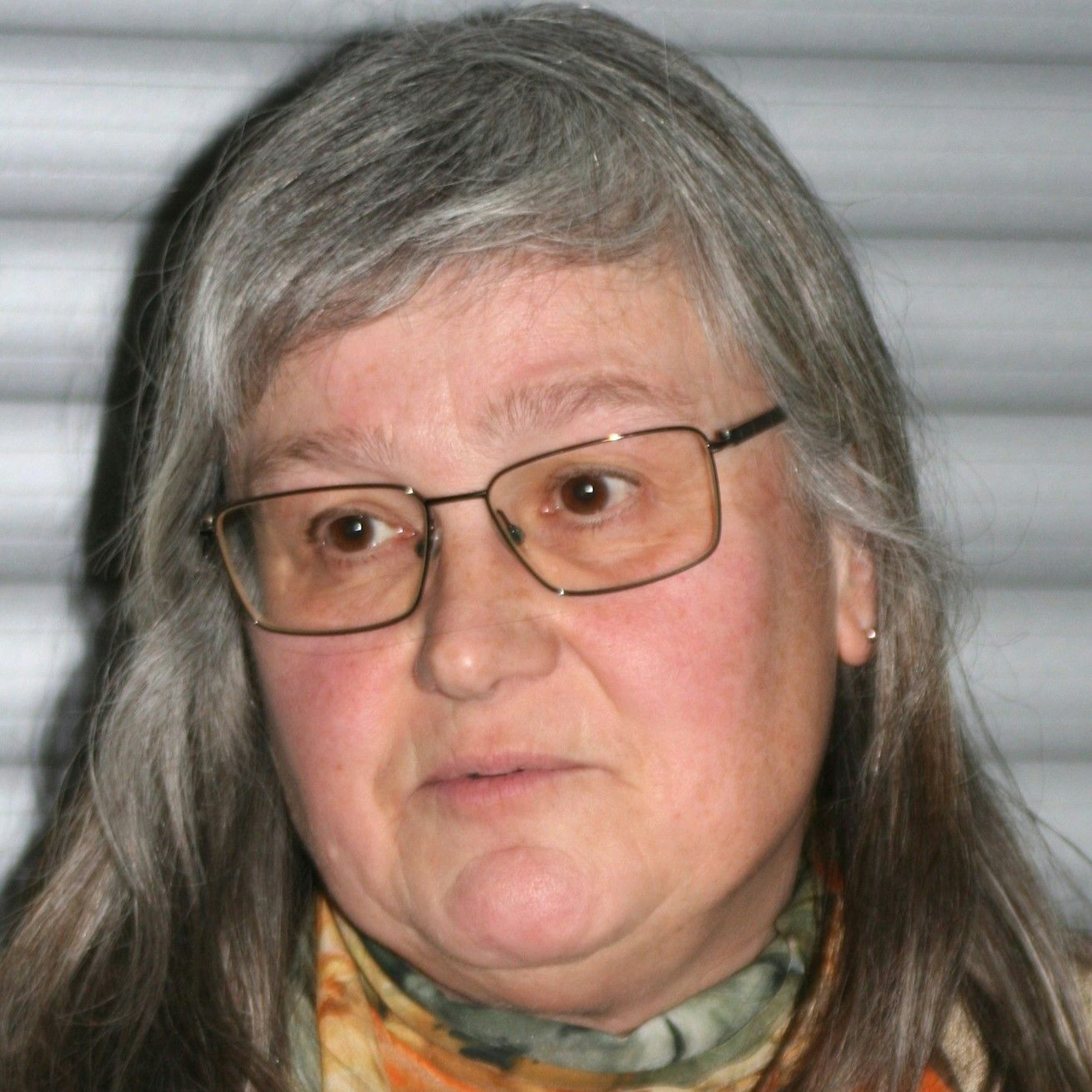 Eine Frau mit langen grauen Haaren und einer Brille. Sie trägt ein buntes Halstuch.