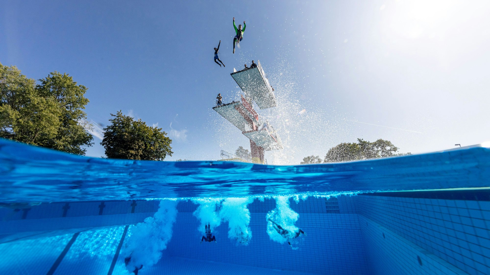 Menschen springen von einem Sprungturm in ein Schwimmbecken.