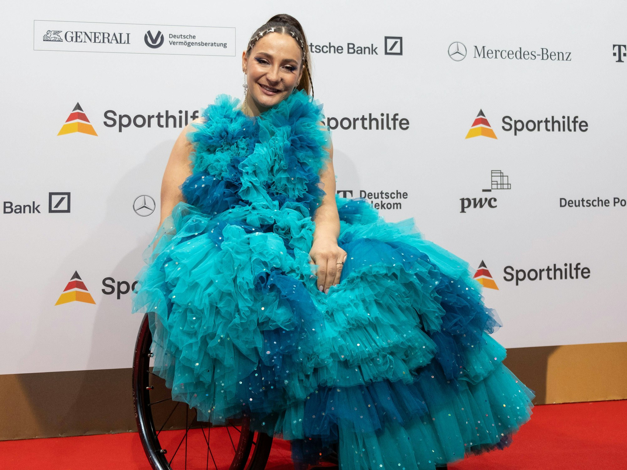 Bahnrad-Olympiasiegerin Kristina Vogel in einem blau-türkisen Kleid mit Rollstuhl auf dem Roten Teppich.
