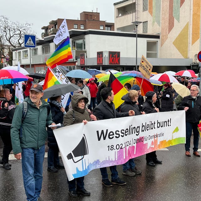 Auf dem Foto sind Teilnehmer der Demonstration gegen Rechtsextremismus in Wesseling zu sehen. Auf einem Banner steht „Wesseling bleibt bunt!“
