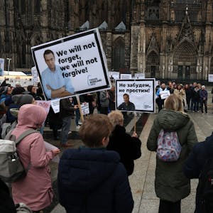 Menschen mit Plakaten stehen in Köln auf der Domplatte.