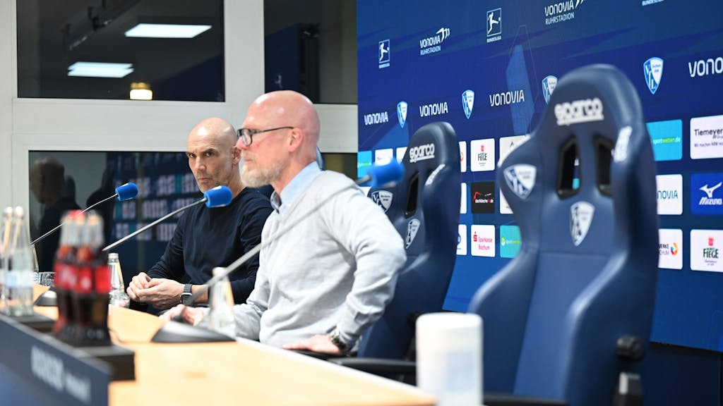 Bochums Trainer Thomas Letsch (l) und Bochums Pressesprecher Jens Fricke sitzen in der Pressekonferenz nach dem Spiel, der rechte Platz von Münchens Cheftrainer Tuchel ist leer.