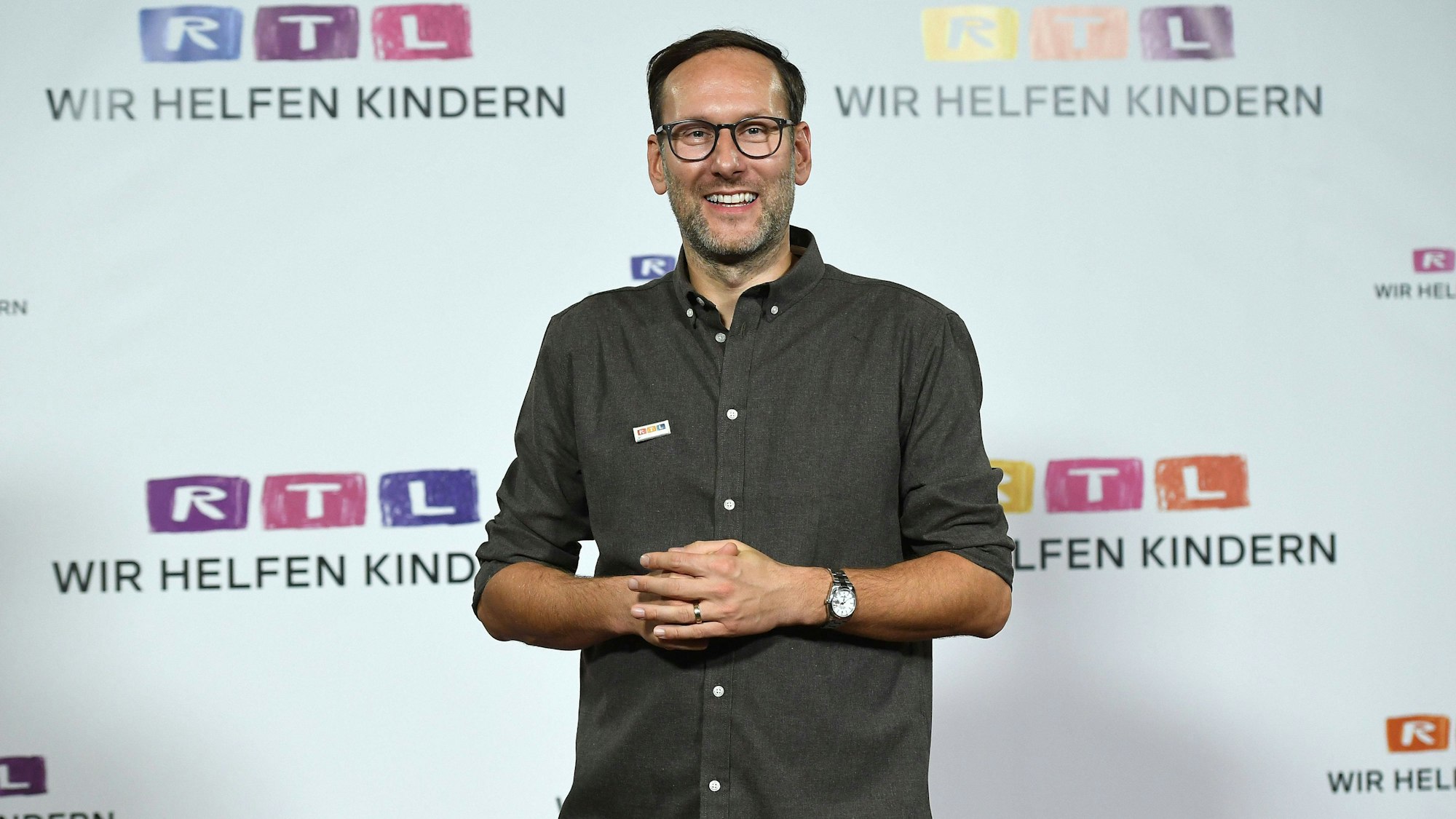 Das Foto zeigt Moderator Simon Beeck beim RTL-„Spendenmarathon“, wo er vor einer Wand voller Logos des Kölner Privatsenders steht.