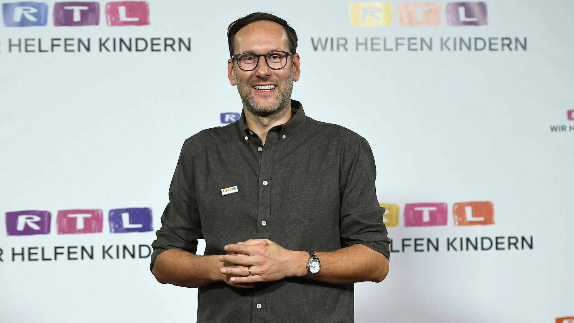 Das Foto zeigt Moderator Simon Beeck beim RTL-„Spendenmarathon“, wo er vor einer Wand mit Logos des Senders steht.