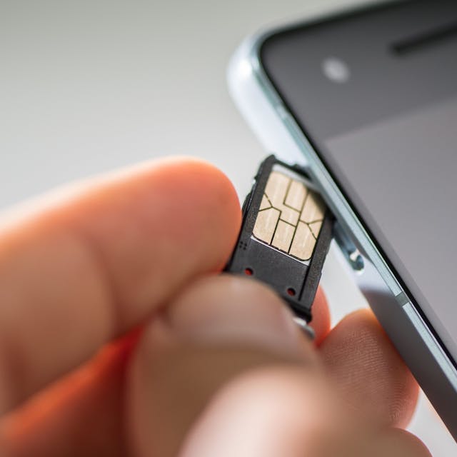Eine Hand führt eine SIM-Karte in ein Smartphone ein.