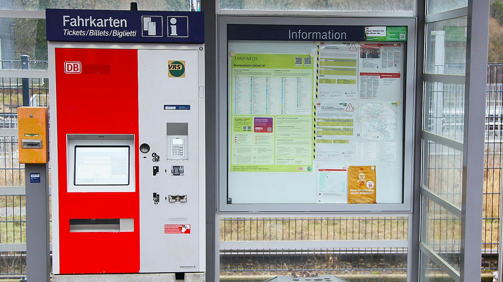 Das Bild zeigt einen Fahrkartenautomaten und Informations-Aushänge am Bahnhof Blankenheim-Wald.