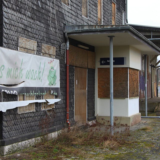 Ein Plakat mit der Aufschrift „Küss mich wach“ hängt an der Fassade des Bahnhofs Blankenheim-Wald. Der untere Teil ist bereits zerrissen.