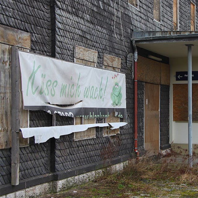Ein Plakat mit der Aufschrift „Küss mich wach“ hängt an der Fassade des Bahnhofs Blankenheim-Wald. Der untere Teil ist bereits zerrissen.