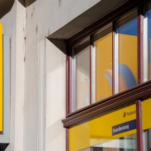 Ein Schild mit dem Logo der Postbank ist an der Fassade einer Bankfiliale angebracht.