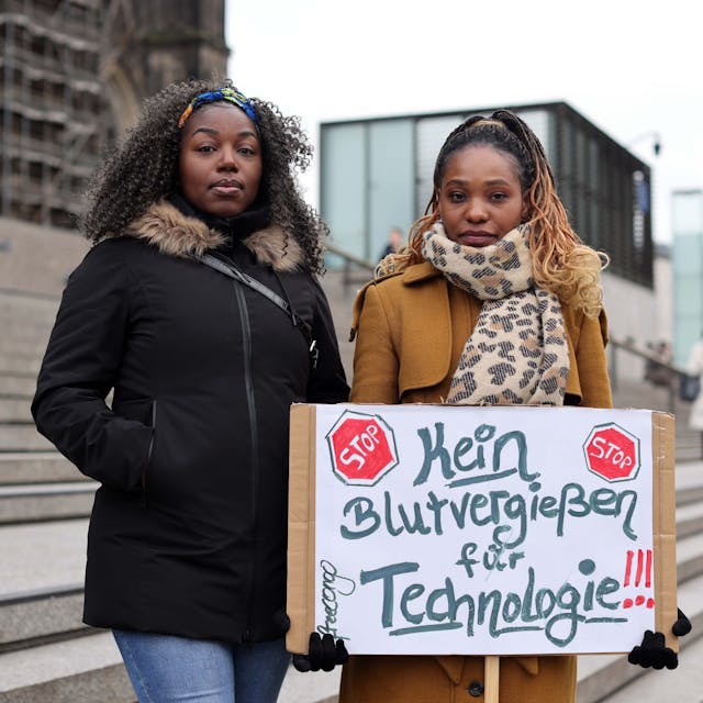 Zwei Frauen halten ein Schild mit der Aufschrift „Kein Blutvergießen für Technologie“.&nbsp;