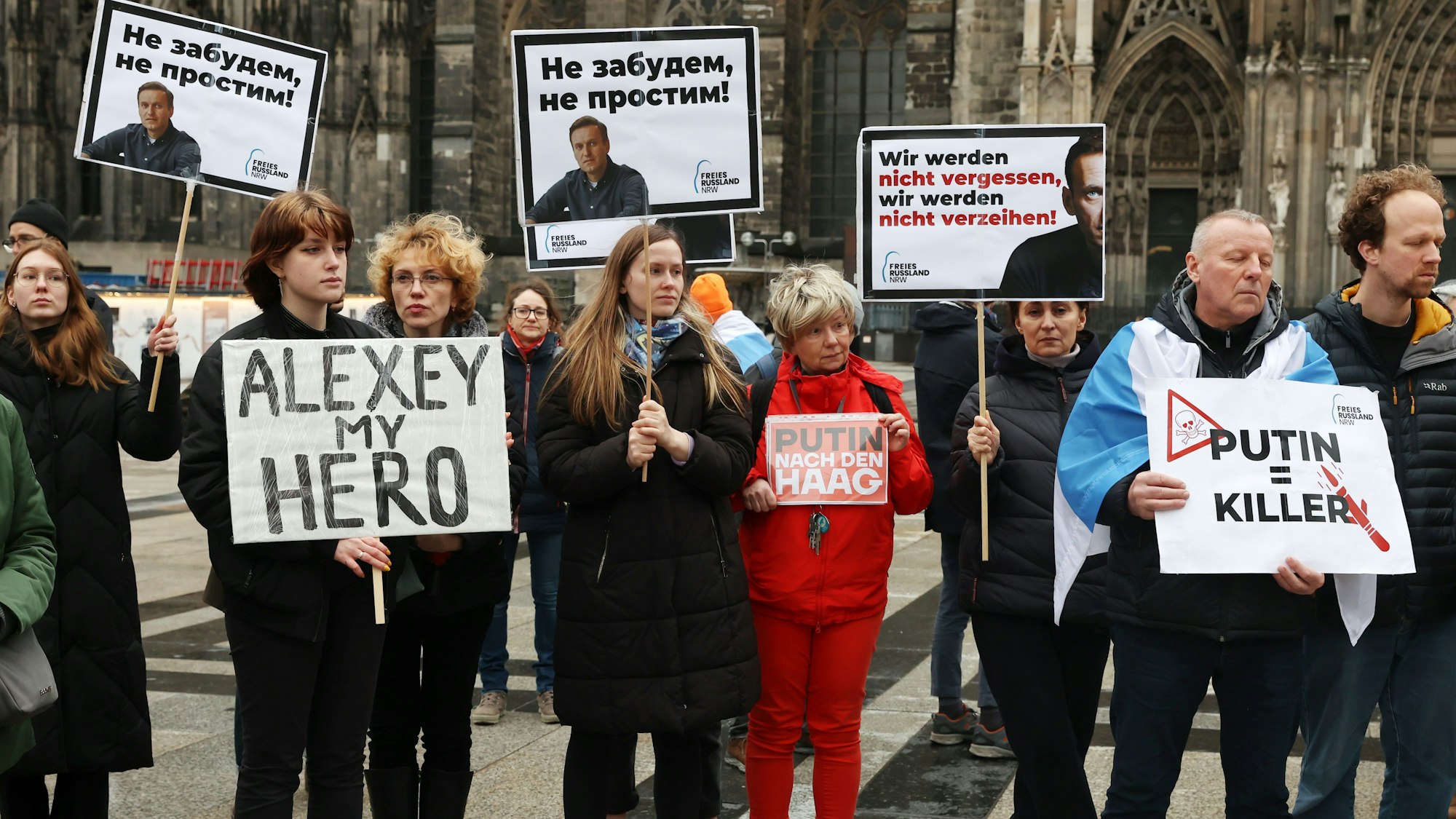 Menschen stehen mit Plakaten vor dem Kölner Dom und gedenken des verstorbenen Alexej Nawalny.


