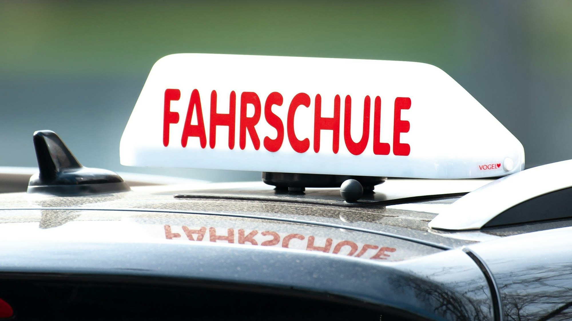 Das Foto zeigt ein Schild mit der Aufschrift „Fahrschule“ auf einem Fahrschulauto.