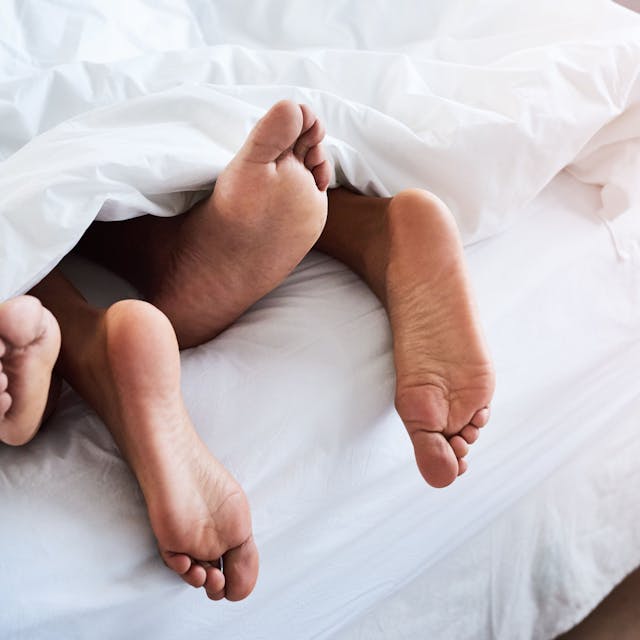 Die Füße eines Paares schauen unter einer Bettdecke hervor.