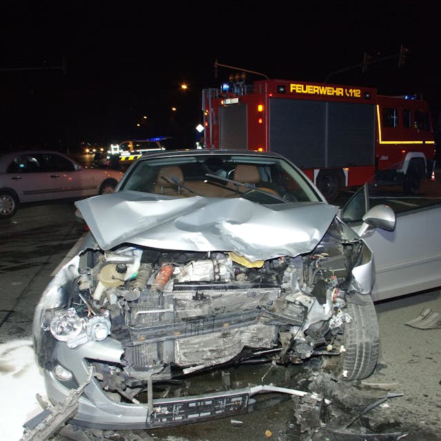 Das Bild zeigt einen beschädigten Wagen vor einem Feuerwehrfahrzeug.