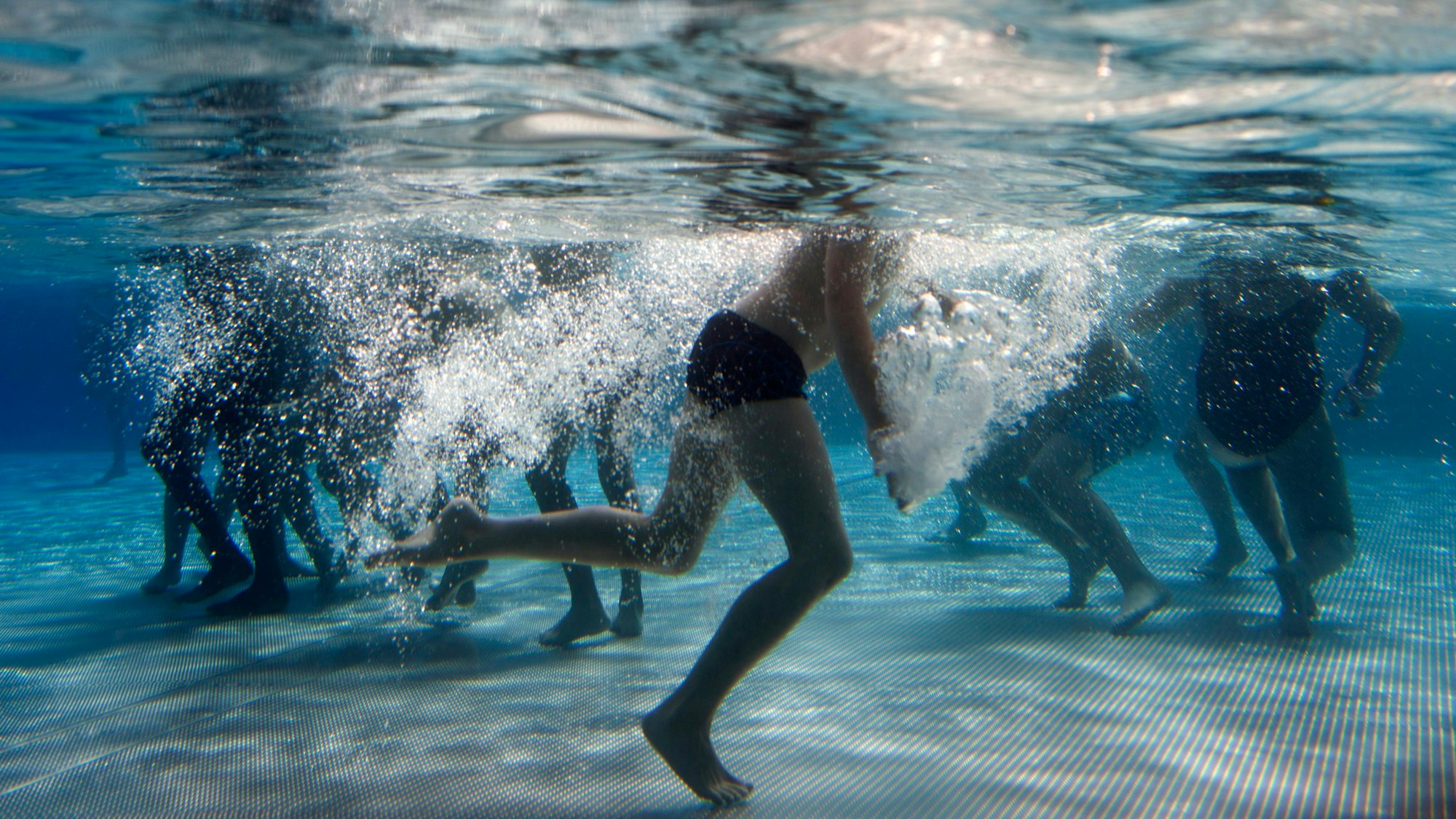 Unter Wasser sind die Beine von schwimmenden Kindern in einem Schwimmbad zu sehen.