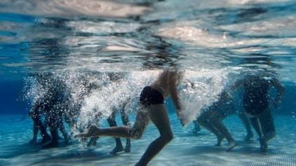 Unter Wasser sind die Beine von schwimmenden Kindern in einem Schwimmbad zu sehen.&nbsp;