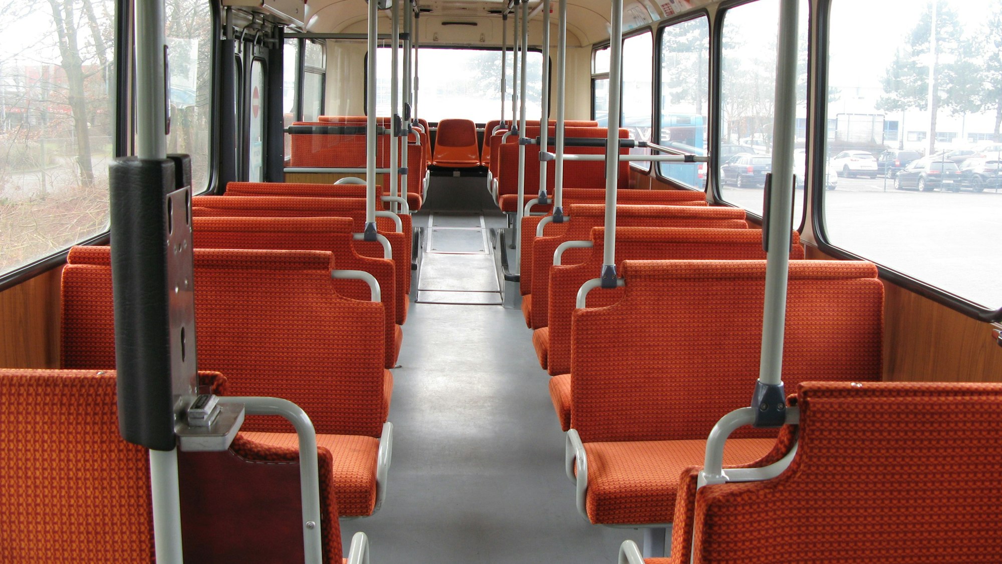Der Blick ins Innere des Busses zeigt den Gang, Haltestangen und die Sitzbänke, die mit einem leuchtend-orangefarbenen Stoff bezogen sind.