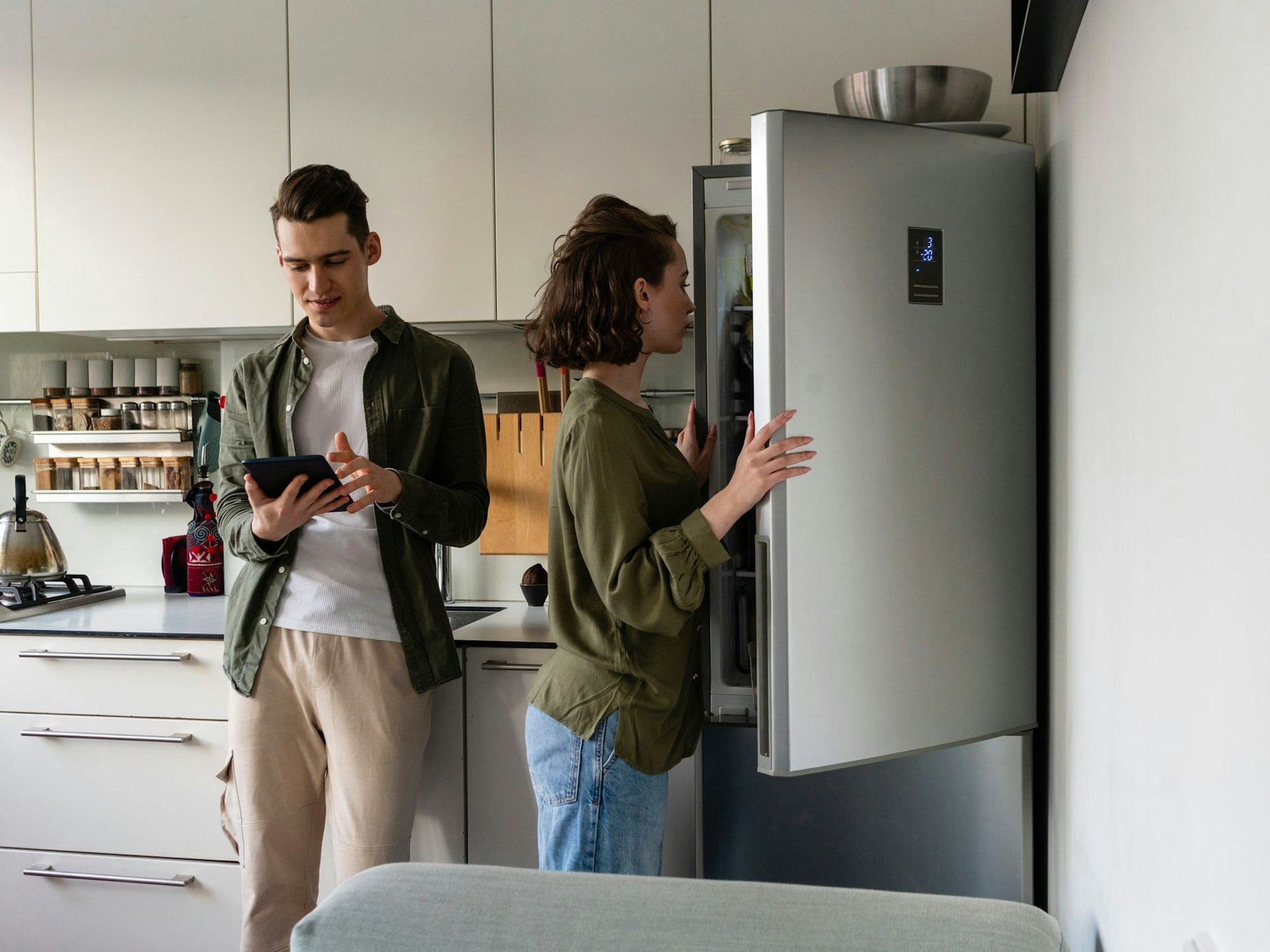 Auf dem Foto sieht man eine Frau einen Kühlschrank öffnen, neben ihr steht ein Mann, welcher auf sein Tablet schaut.
