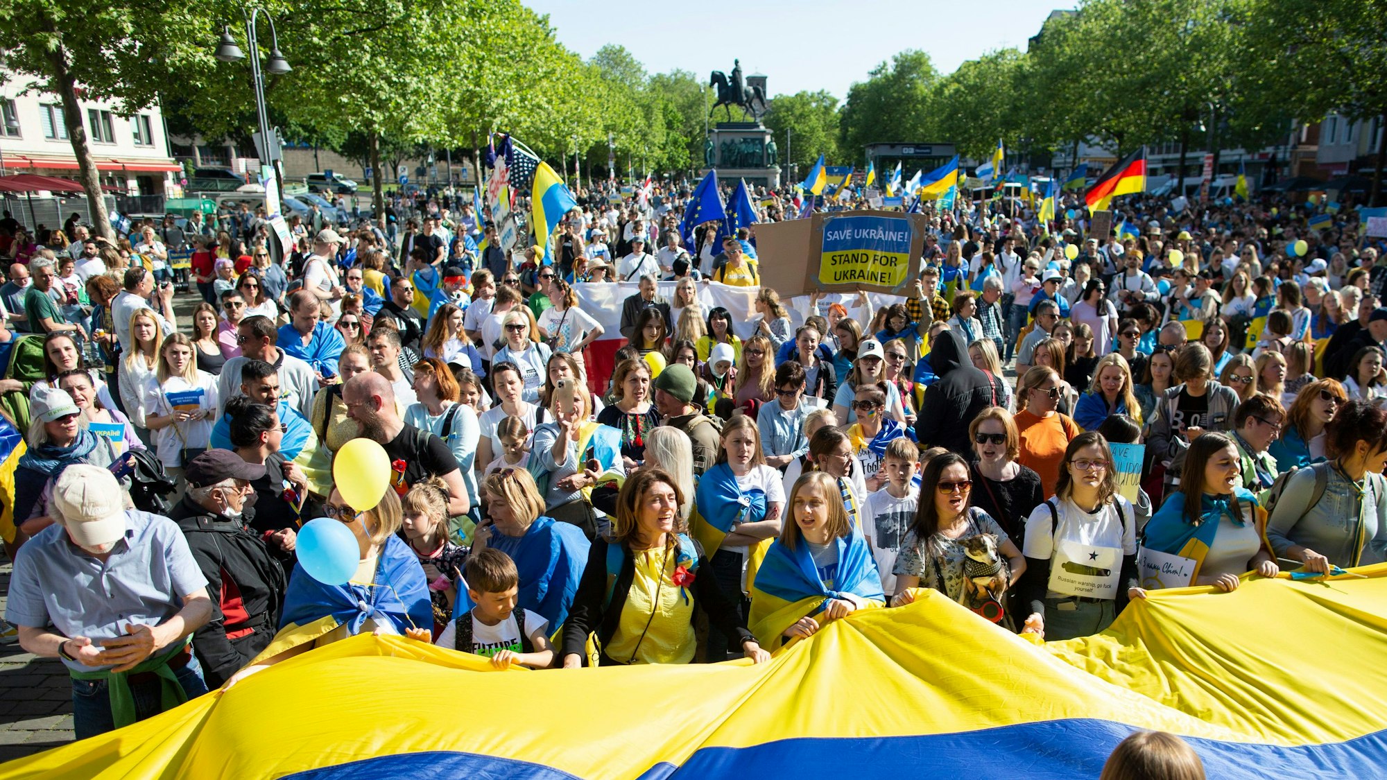Bei einer Demo in Köln wird ein Banner in den Farben der ukrainischen Flagge gehalten.
