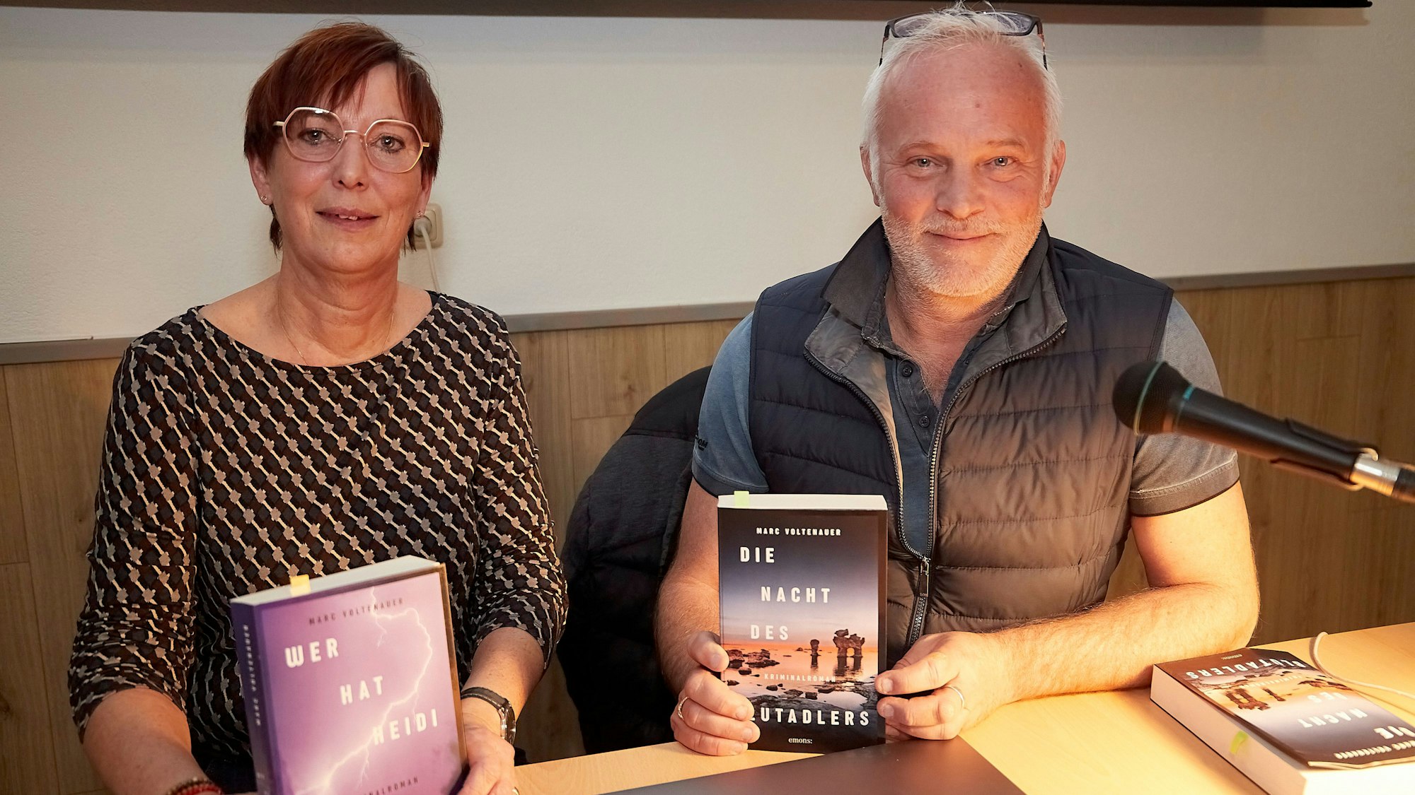 Ein Mann und eine Frau, Übersetzerin Franziska Weyer und der Schweizer Autor Marc Voltenauer, sitzen an einem Tisch. Beide halten ein Buch in der Hand.