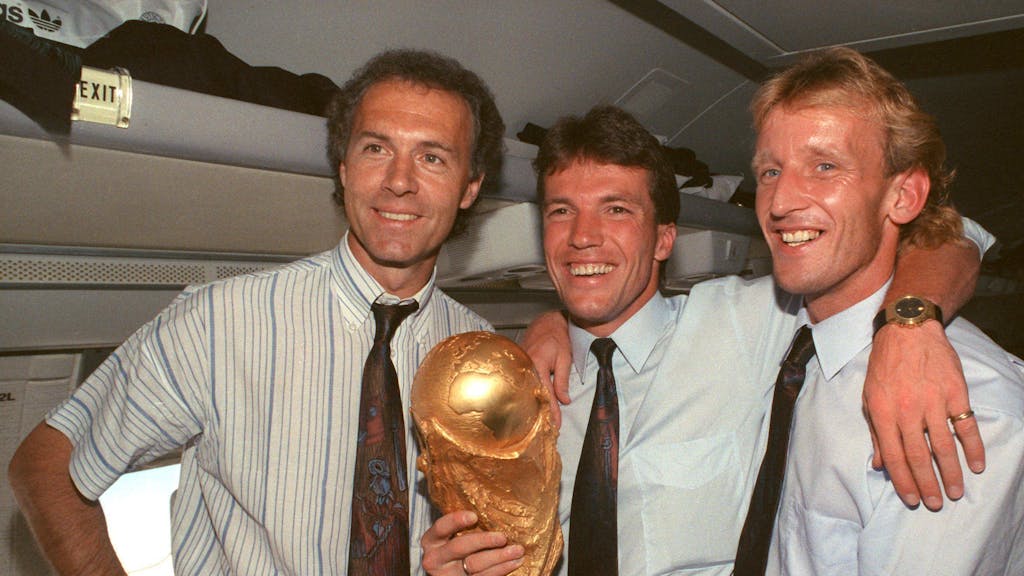 Franz Beckenbauer, Lothar Matthäus und Andreas Brehme halten auf dem Flug von Rom nach Frankfurt den WM-Pokal in der Hand.