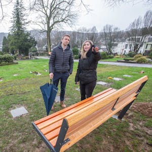 Ein Mann und eine Frau stehen vor einer Bank auf dem Friedhof.