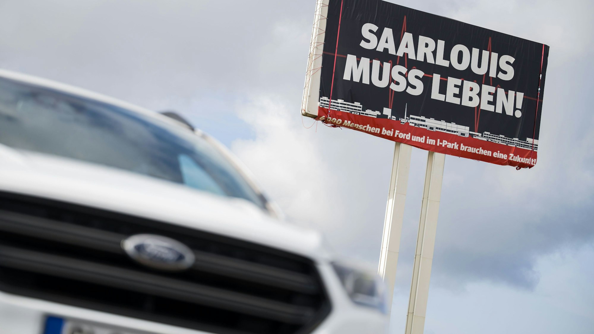 Ein Ford Kuga steht vor einem großen Schild, auf dem für die Bedeutung des Ford Werks in Saarlouis geworben wird. Bei einer Betriebsversammlung hofft die Belegschaft mehr über die Zukunft des Werkes zu erfahren.