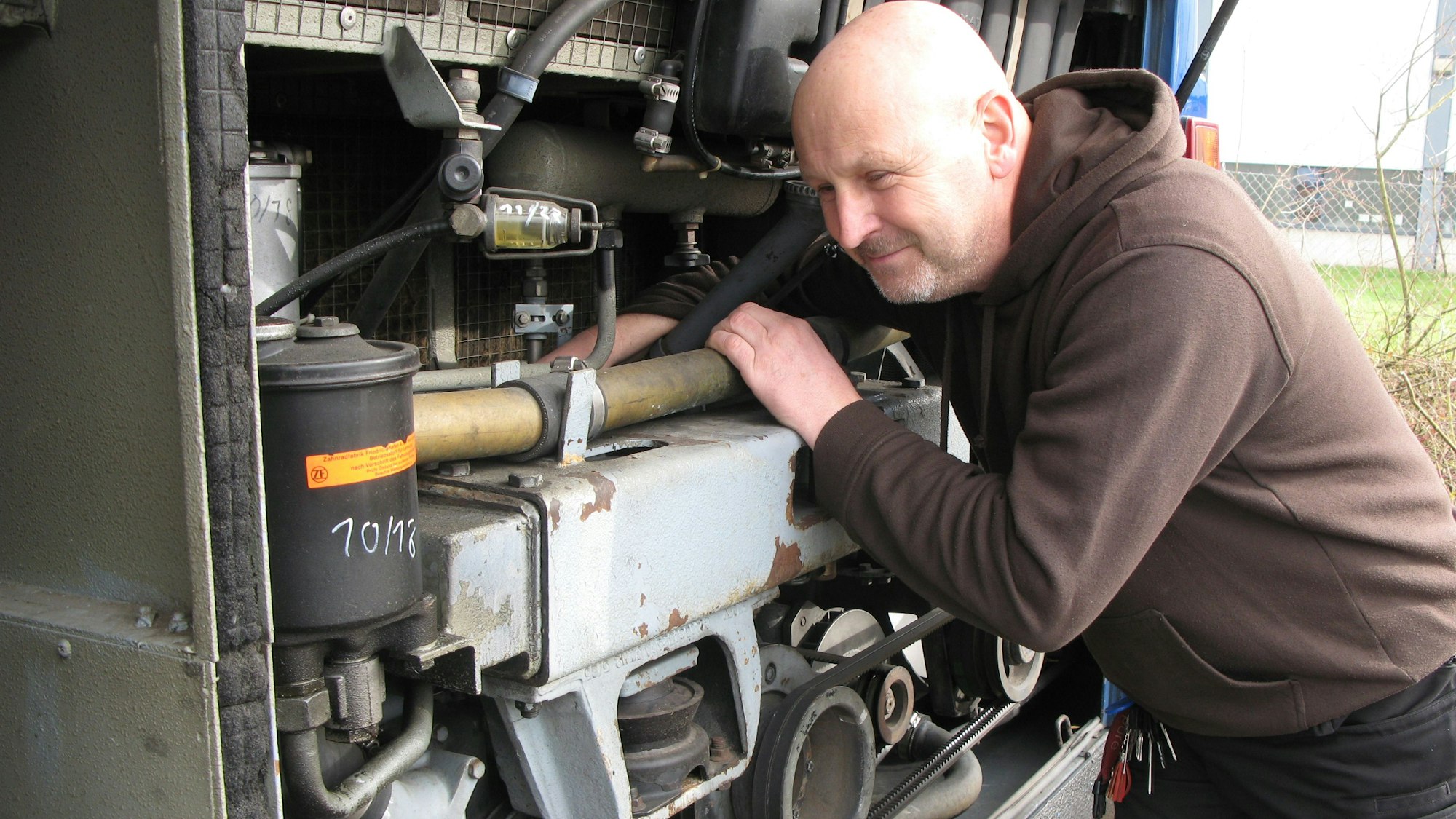 Der Werkstattmeister Robert Geßner steht unter der geöffneten Motorklappe am Heck des Busses und greift mit einer Hand in den Motorraum.