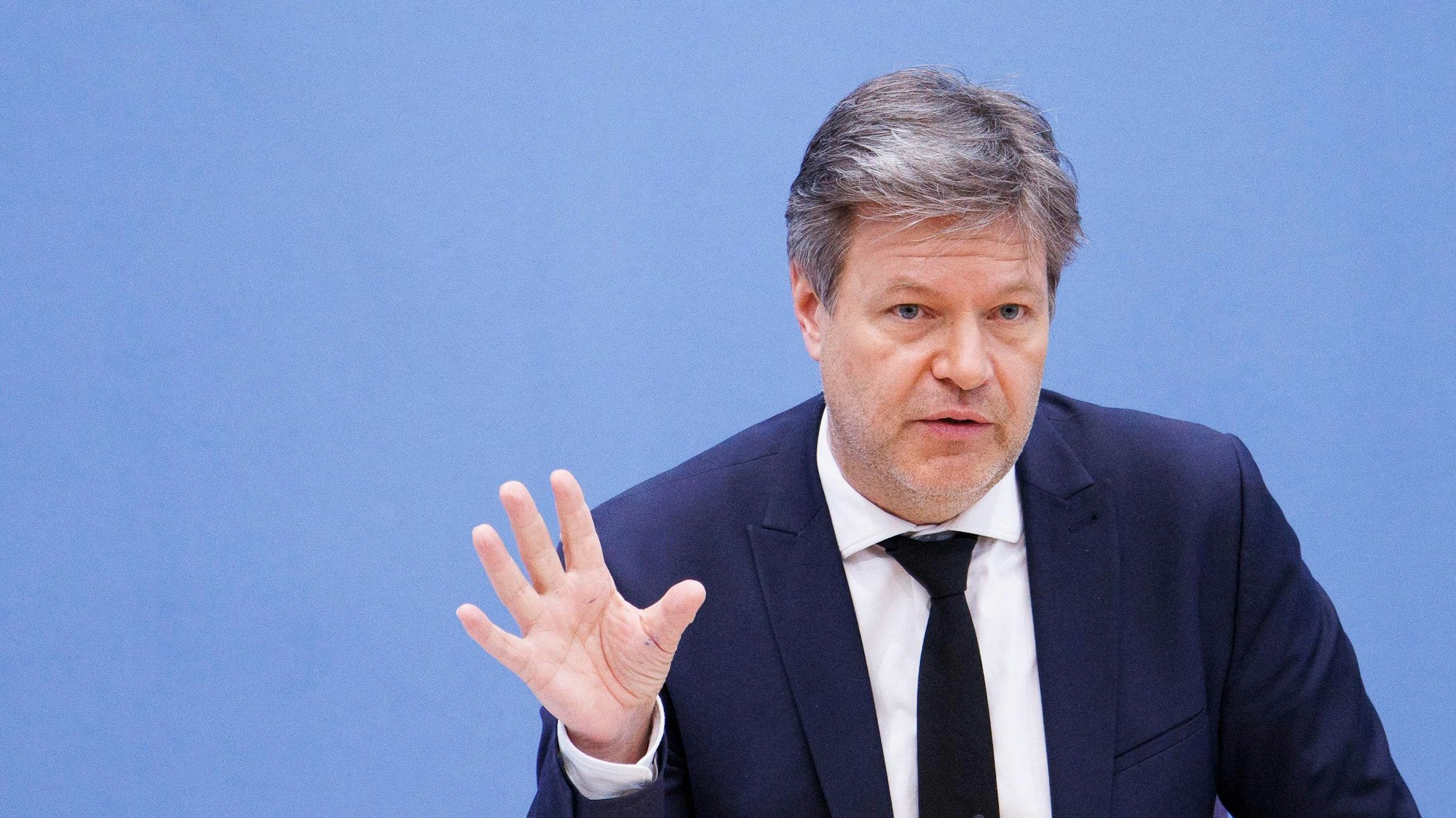 Robert Habeck (Bündnis 90/Die Grünen), Bundesminister für Wirtschaft und Klimaschutz, artikuliert mit der rechten, offenen Hand vor einem blauen Hintergrund.