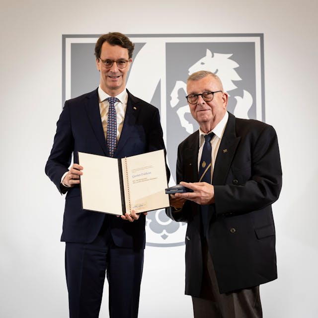 Ministerpräsident Hendrik Wüst hält eine Urkunde in der Hand, Günter Dahlem aus Euskirchen den Landesverdienstorden.