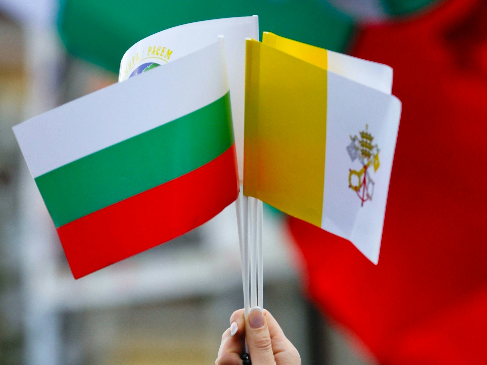 Eine Frau hält die Flaggen von Bulgarien und dem Vatikan hoch.