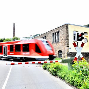Ein Zug der Regionalbahn 25 passiert den Bahnübergang Märkische Straße in Engelskirchen, im Hintergrund die Fabrik Ermen und Engels, wo heute das Industriemuseum und das Rathaus zu finden sind.