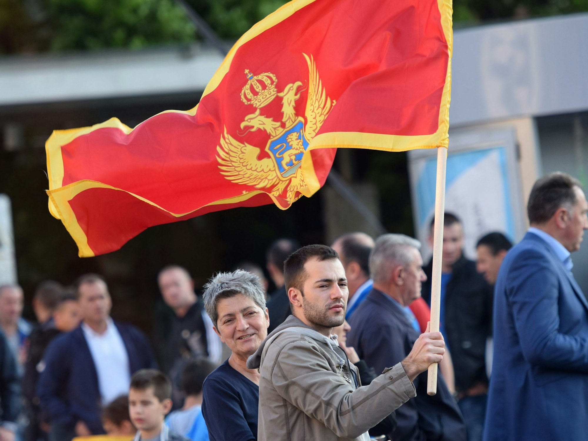 Ein Mann hält eine große Flagge von Montenegro hoch.