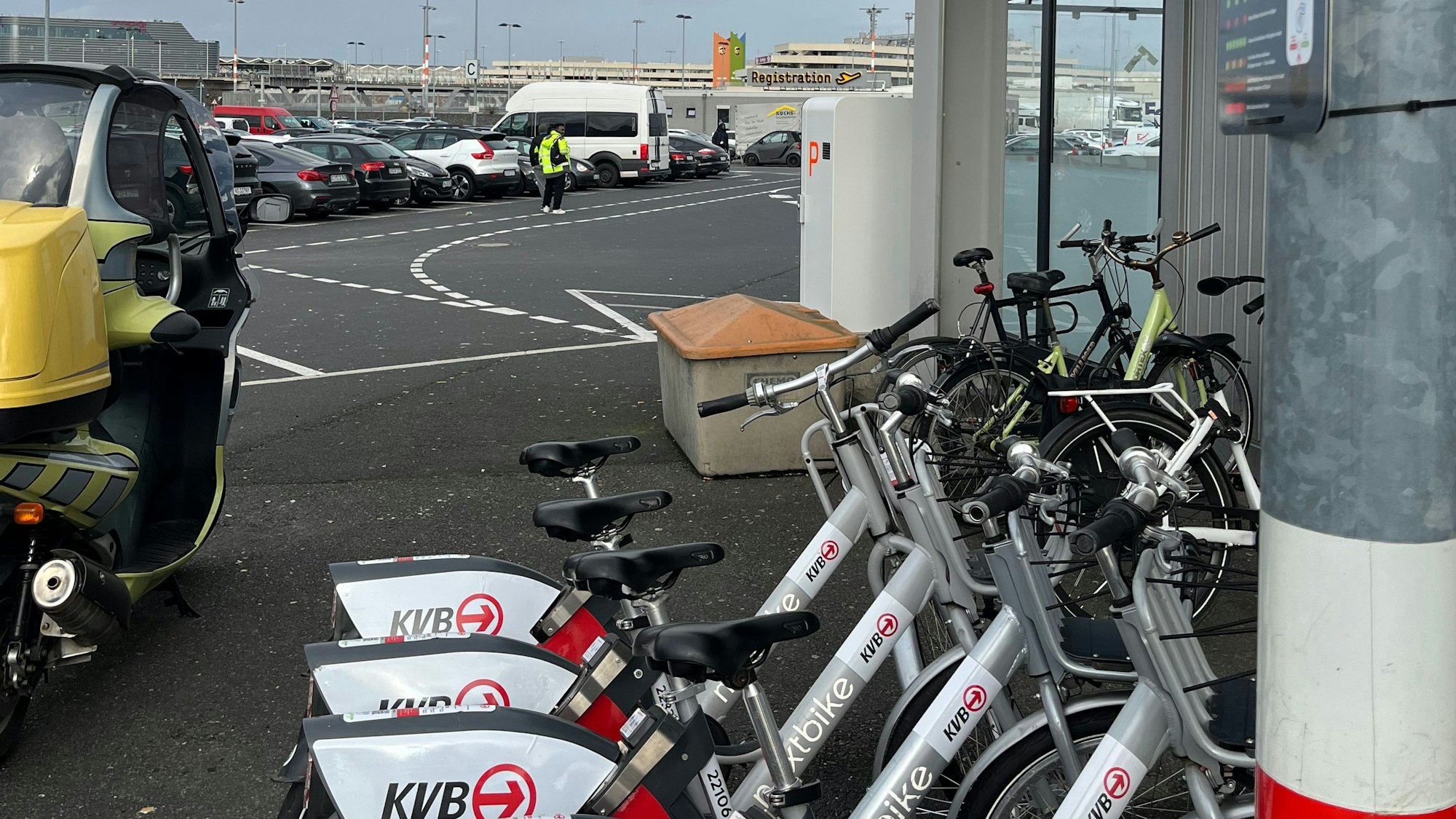 Leihräder mit der Aufschrift „KVB“ auf einem Parkplatz, im Hintergrund sieht man den Flughafen Köln/Bonn