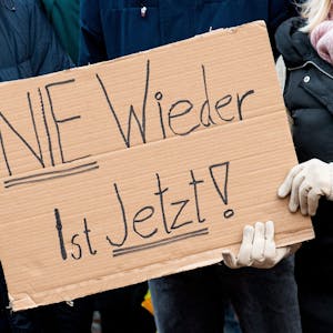 Teilnehmer einer Demonstration gegen Rechtsextremismus halten ein Schild „Nie wieder ist jetzt" in Händen.&nbsp;