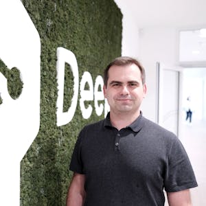 Jaroslaw Kutylowski, Chef von DeepL, steht in der Kölner Zentrale vor einem Logo der Firma.