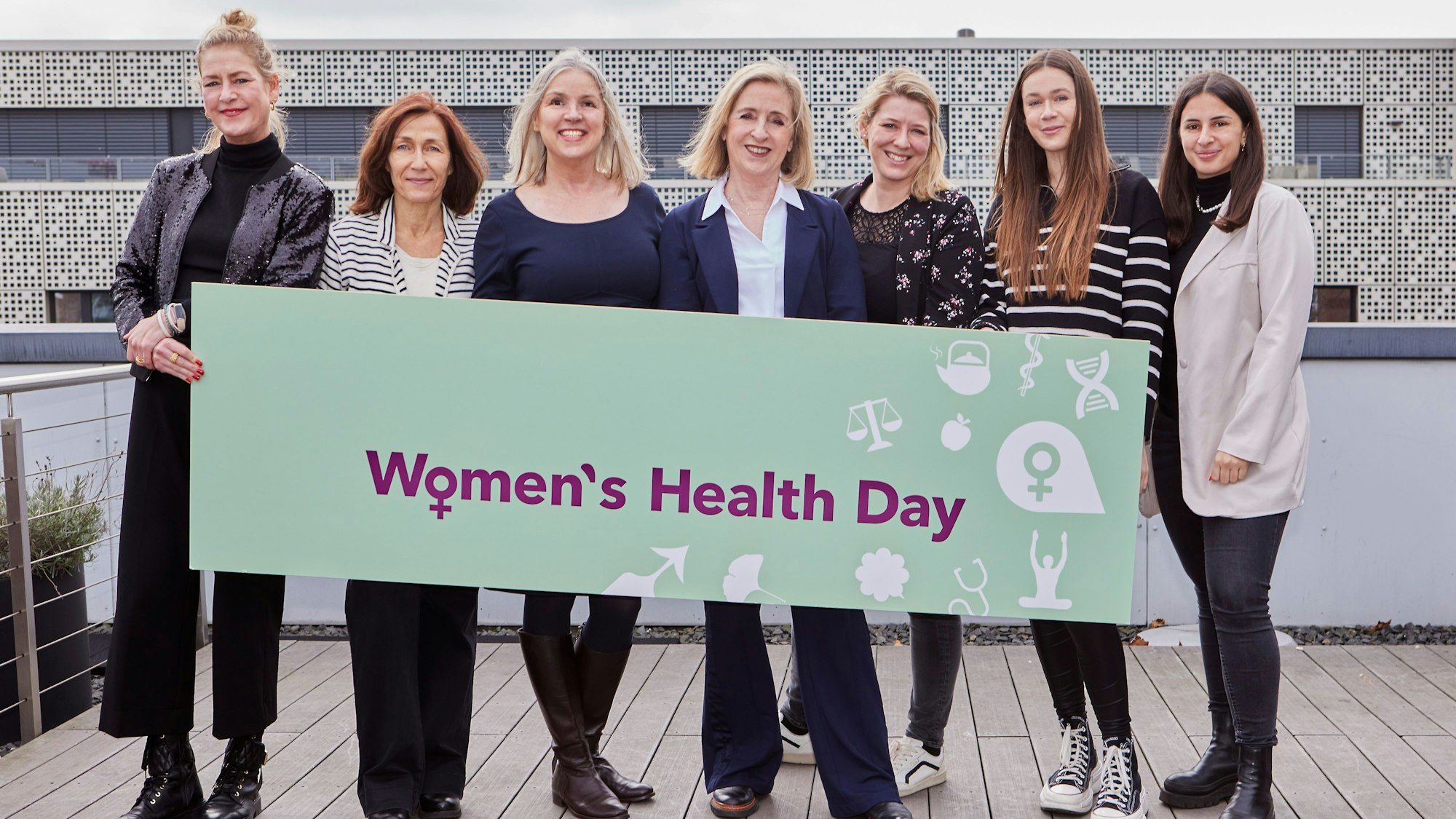Sechs Frauen halten gemeinsam ein waagerechtes Plakat mit dem Slogan „Women's Health Day“.